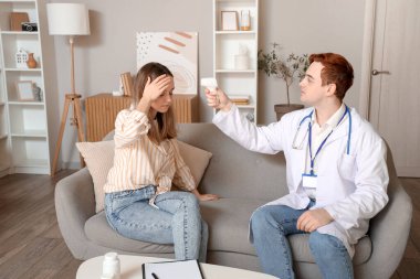 Erkek doktor, evdeki genç kadının ateşini ölçüyor.