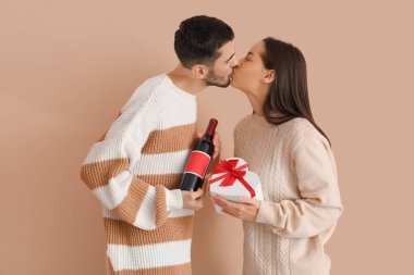 Bir şişe şarabı olan ve bej arka planda öpüşen mutlu genç bir çift. Sevgililer Günü kutlaması