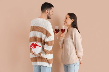 Şarap kadehleri ve bej arka planda hediyeleri olan mutlu genç bir çift. Sevgililer Günü kutlaması