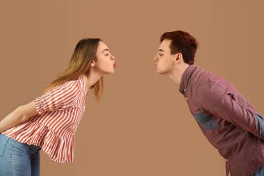 Genç çift kahverengi arka planda öpüşüyor.