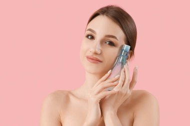 Pembe arka planda bir şişe kozmetik ürünü olan güzel genç bir kadın.