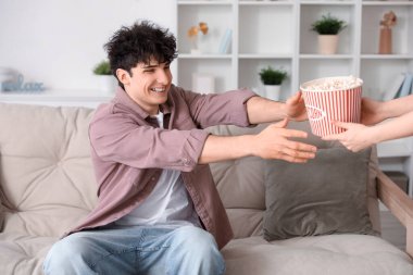 Genç adam film izliyor ve oturma odasındaki kanepede patlamış mısır yiyor.