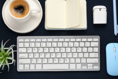 Fare, kulaklık, kahve fincanı ve siyah arka planda not defteri olan modern bilgisayar klavyesi.
