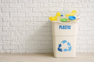 Beyaz tuğla duvarın yanında PLASTIC işareti olan tam çöp kutusu. Geri dönüşüm kavramı
