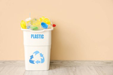 Bej duvarın yanında PLASTIC işareti olan tam çöp kutusu. Geri dönüşüm kavramı