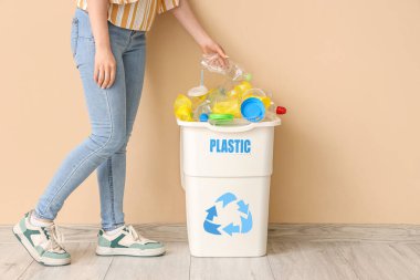 Kadın, bej duvarın yanında plastiklerle dolu bir çöp kutusuna koyuyor. Geri dönüşüm kavramı