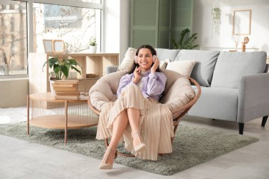 Kulaklıklı genç ve güzel bir kadın. Sesli kitap dinliyor ve oturma odasında koltukta oturuyor.