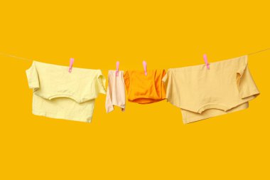 Sarı arka planda ipte asılı temiz giysiler.