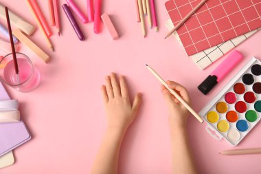 Pembe arka plan üzerine çizim yapmak için farklı kırtasiye malzemesi olan çocuk elleri