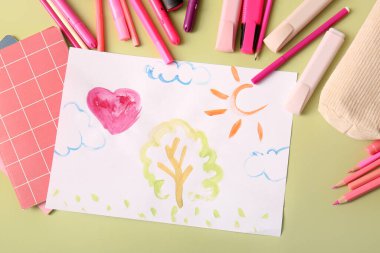 Kalemleri, defterleri ve yeşil arka planda renkli kalemleri olan çocuk çizimleri.