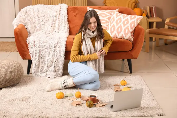 Sonbahar günü dizüstü bilgisayarı olan genç bir kadın evde oturuyor.