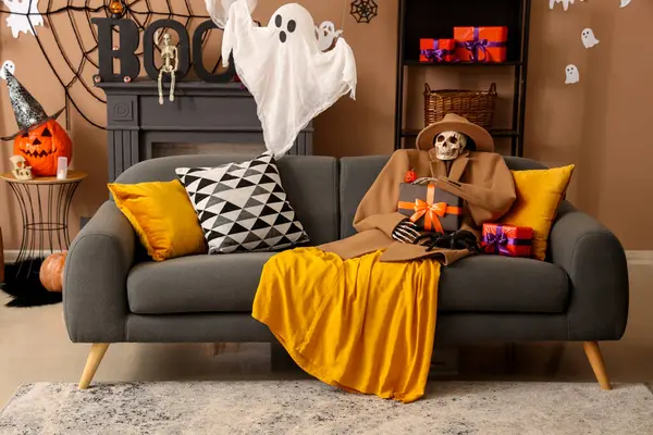 Sonbahar kıyafetleri içinde korkunç Cadılar Bayramı iskeleti hediye kutusu ve oturma odasındaki kanepede oturan tarantula.