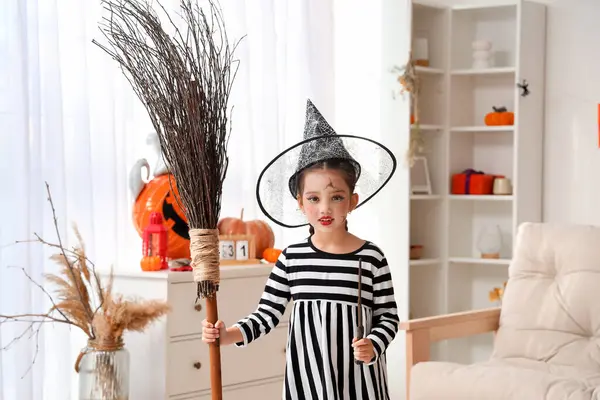 Evde süpürgeyle cadılar bayramını kutlayan küçük kız.