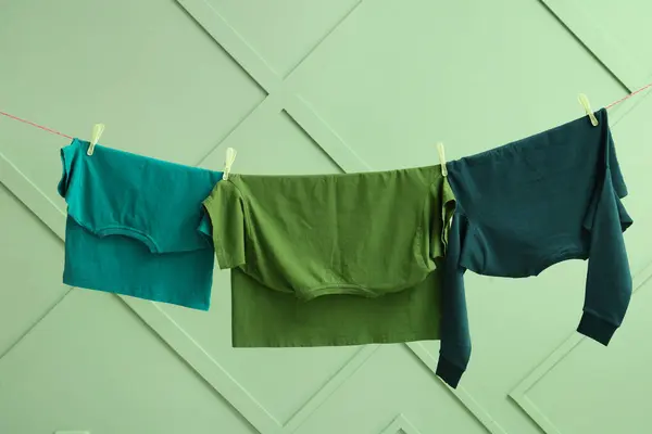 stock image Clean clothes hanging on rope against color wall