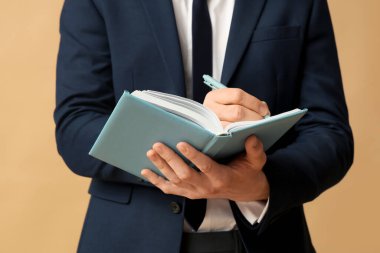 Kahverengi arka planda defteri olan genç işadamı, yakın plan.