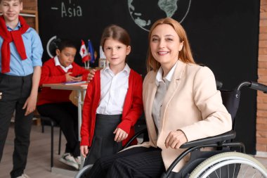 Tekerlekli sandalyedeki olgun coğrafya öğretmeni okuldaki küçük kıza sarılıyor.