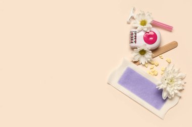 Tıraş makinesi, balmumu şeridi ve bej arka planda çiçekler.