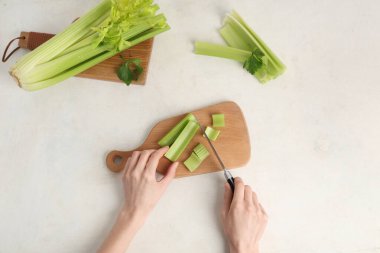 Beyaz arka planda taze yeşil kereviz kesen kadın.