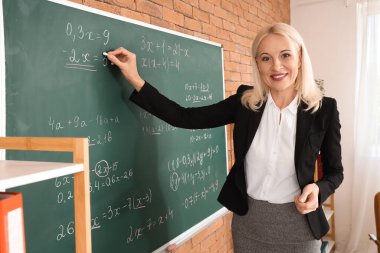 Sınıfta tahtaya yazı yazan kadın matematik öğretmeni.