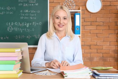 Sınıftaki kadın matematik öğretmeni, kitapçığı kontrol ediyor.