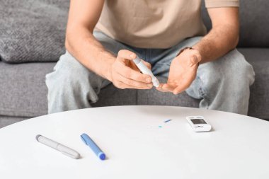 Şeker hastası genç adam evdeki kanepede tükenmez kalem kullanıyor.