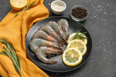Siyah arka planda taze çiğ karides, limon ve biberiye tabağı.