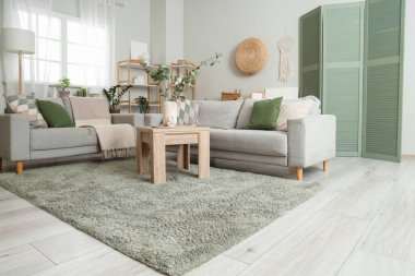 Oturma odasının içinde kanepeler, masa ve yeşil halı var.