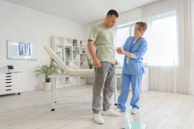 Kadın doktor klinikte erkeğin belini ölçüyor.