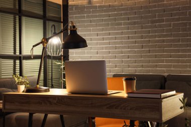 Çalışma odası. Laptop, kahve fincanı ve karanlık ofiste parlayan lamba.