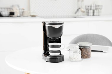 Mutfaktaki masada bir kavanoz kahve, şeker ve fincanlı modern makine.
