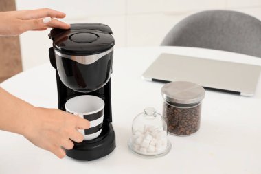 Mutfakta modern makineyle kahve yapan genç ve güzel bir kadın.