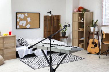 Yatak odasının içinde mikrofon, modern sentezleyici ve gitar var.