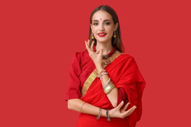 Güzel, genç, mutlu, Hintli bir kadın, kırmızı arka planda dans ediyor.