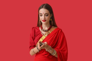 Kırmızı arka planda diya lambası olan şık sarili güzel bir Hintli kadın.