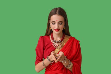 Yeşil arka planda diya lambası olan sarili güzel, mutlu, Hintli bir kadın.