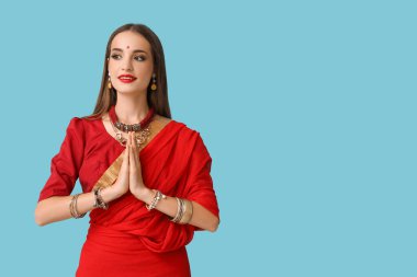 Güzel, genç, mutlu Hintli bir kadın şık bir elbiseyle mavi arka planda dua ediyor.