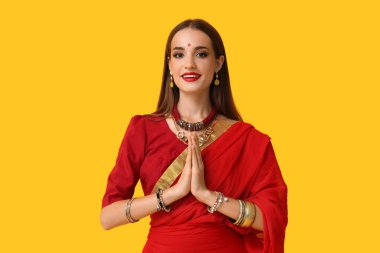 Sarı arka planda dua eden güzel, mutlu, Hintli bir kadın.