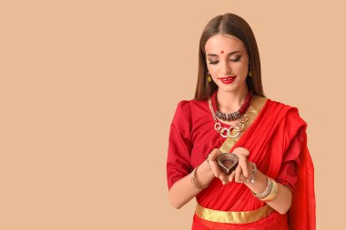 Bej arka planda diya lambası olan sarili güzel, mutlu, Hintli bir kadın.