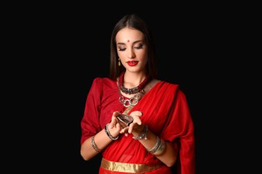 Siyah arka planda diya lambası olan şık sarili güzel bir Hintli kadın.