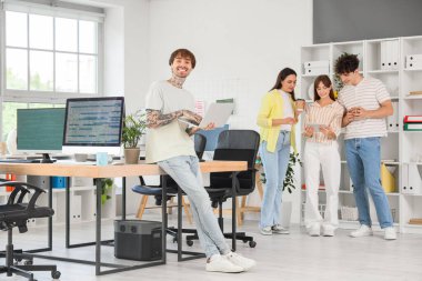 Ofiste dizüstü bilgisayarla çalışan dövmeli erkek programcı.