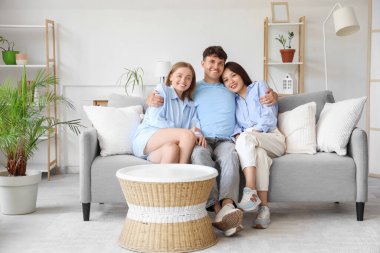 Evdeki kanepede iki kadınla sarılan genç adam. Poliyamory konsepti