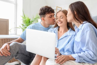 Evde iki kadın ve dizüstü bilgisayarla öpüşen genç bir adam. Poliyamory konsepti