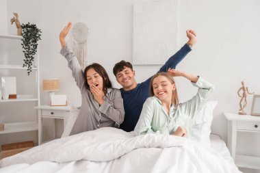 Sleepy young man with two women stretching in bedroom. Polyamory concept clipart