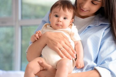 Anne küçük bebeğini pencerenin yanında tutuyor, yakın plan.