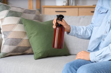 Aroma spreyi şişesi olan kadın evdeki kanepede oturuyor, yakın plan.