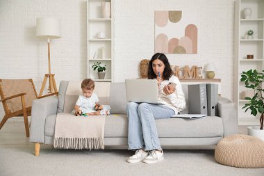 Çalışan anne ve küçük bebeği evdeki kanepede oyuncaklarla oynuyorlar.