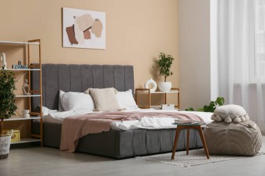 Şık yatak odasının içinde raf üniteleri, puf ve masa var.