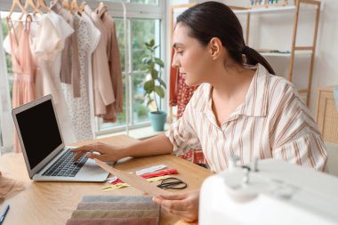 Atölyede dizüstü bilgisayarla çalışan kadın terzi.