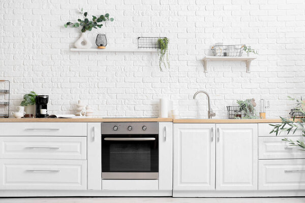 Интерьер светлой кухни с современной кофеваркой, белыми столешницами и комнатными растениями