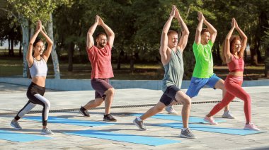 Bir grup genç sporcu dışarıda yoga yapıyor.